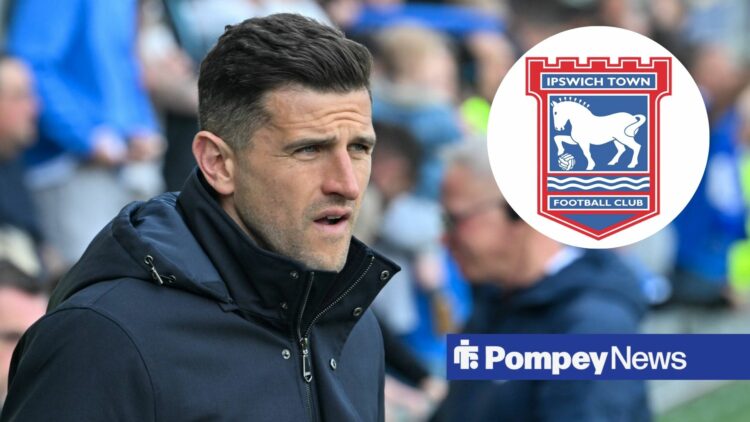John Mousinho wearing coat in dugout with Ipswich badge in circular inset